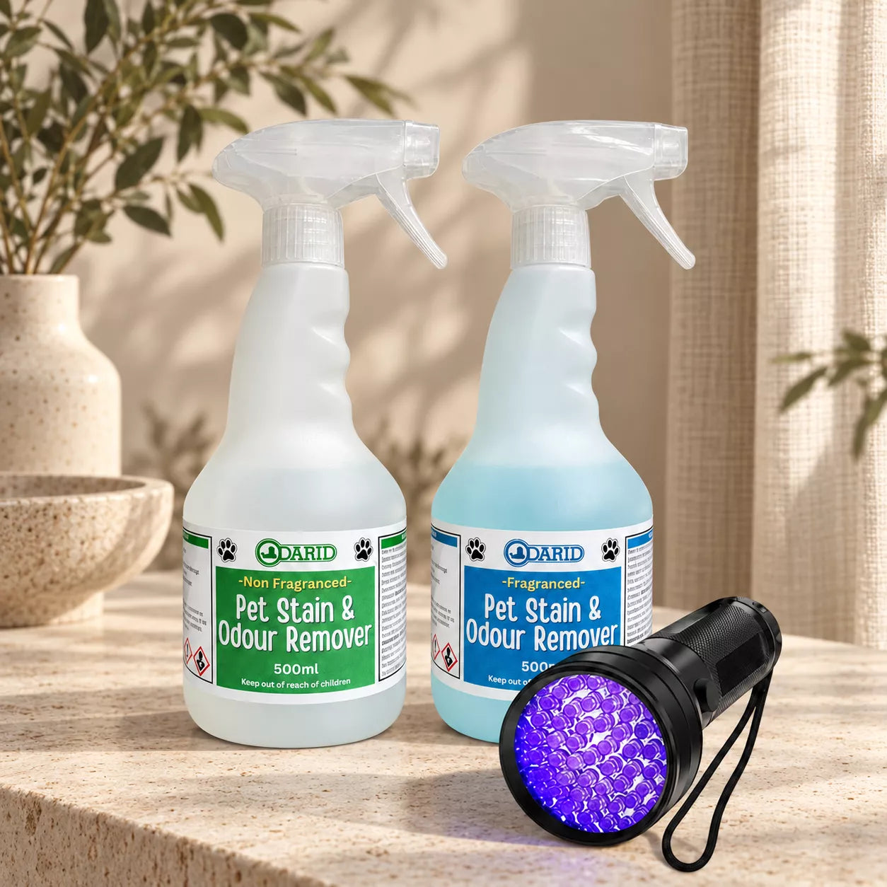 Two 500ml spray bottles of Odarid Pet Stain & Odour Remover, one with a green label and one with a blue label, shown on a stone surface with a black UV light accessory in the foreground.